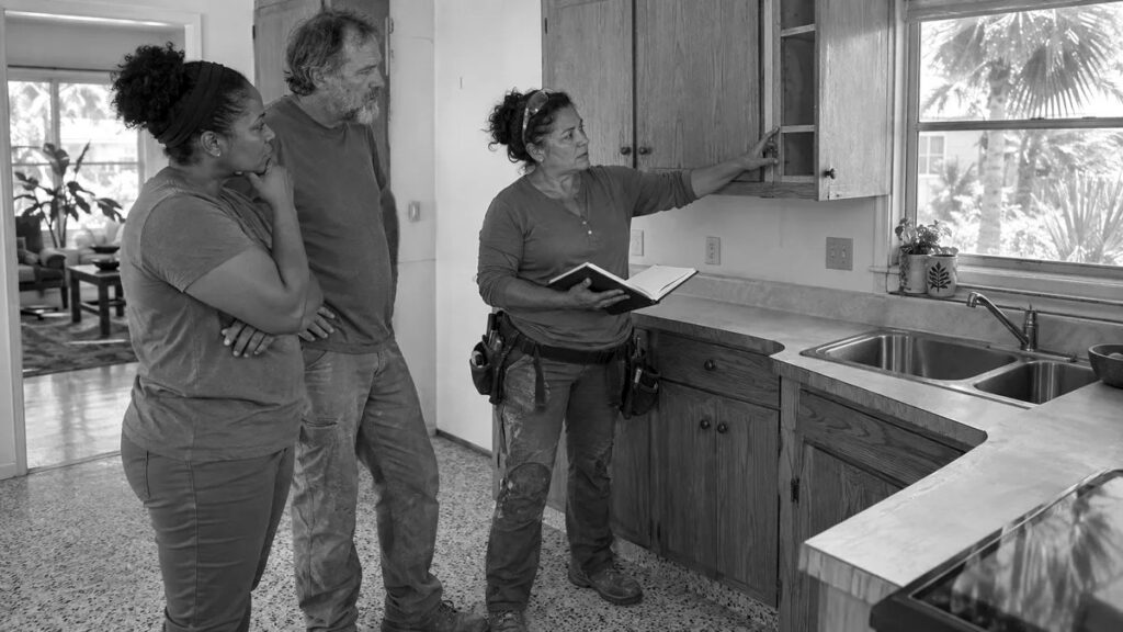 Placeholder image. A remodeler with a notebook showing two homeowners the inside of a dated kitchen cabinet.